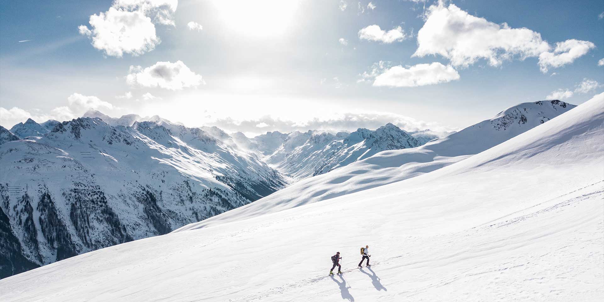 Two people skiing on groomed ski run on sunny day